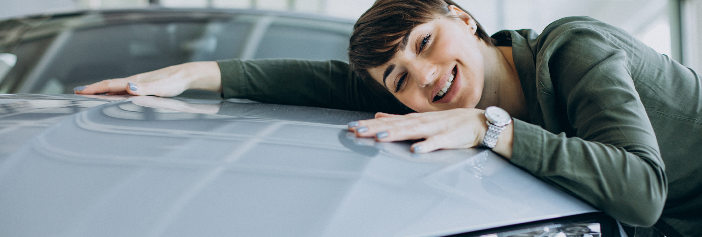 A woman rests her head on the hood of her shiny new car, smiling with satisfaction. She looks proud of her purchase and happy with her choice.