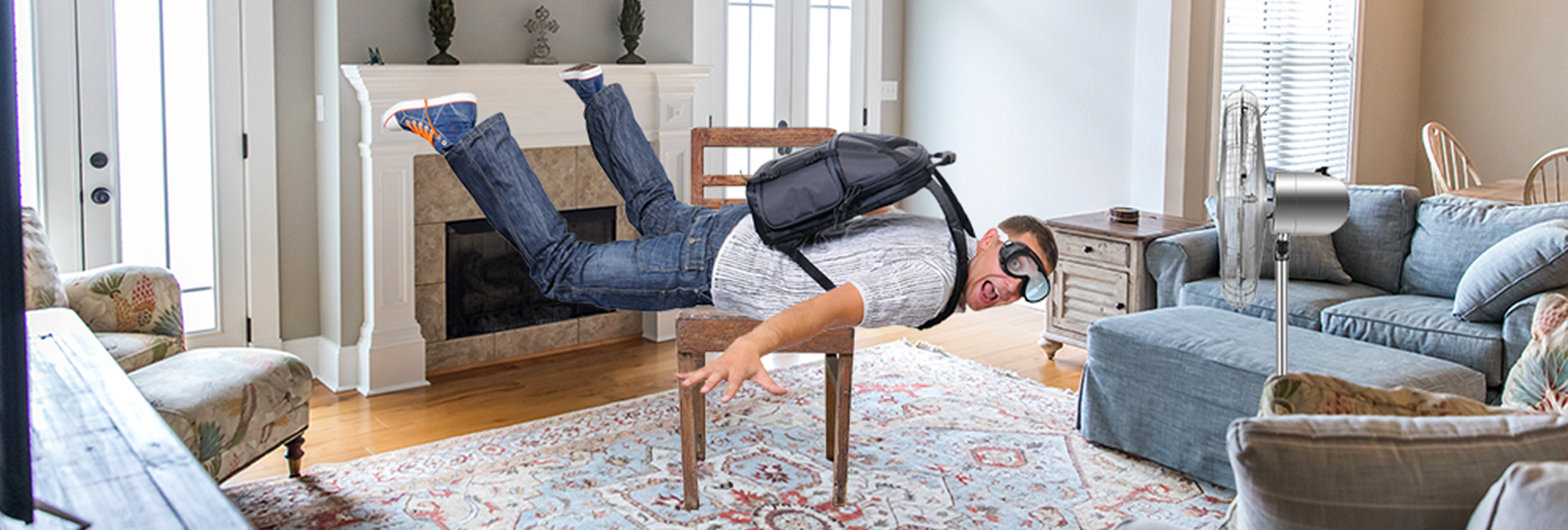 A yound man floating in the air in a cozy living room wearing a backpack and black goggles with a surprised expression on his face as if he did not expect to defy gravity.
