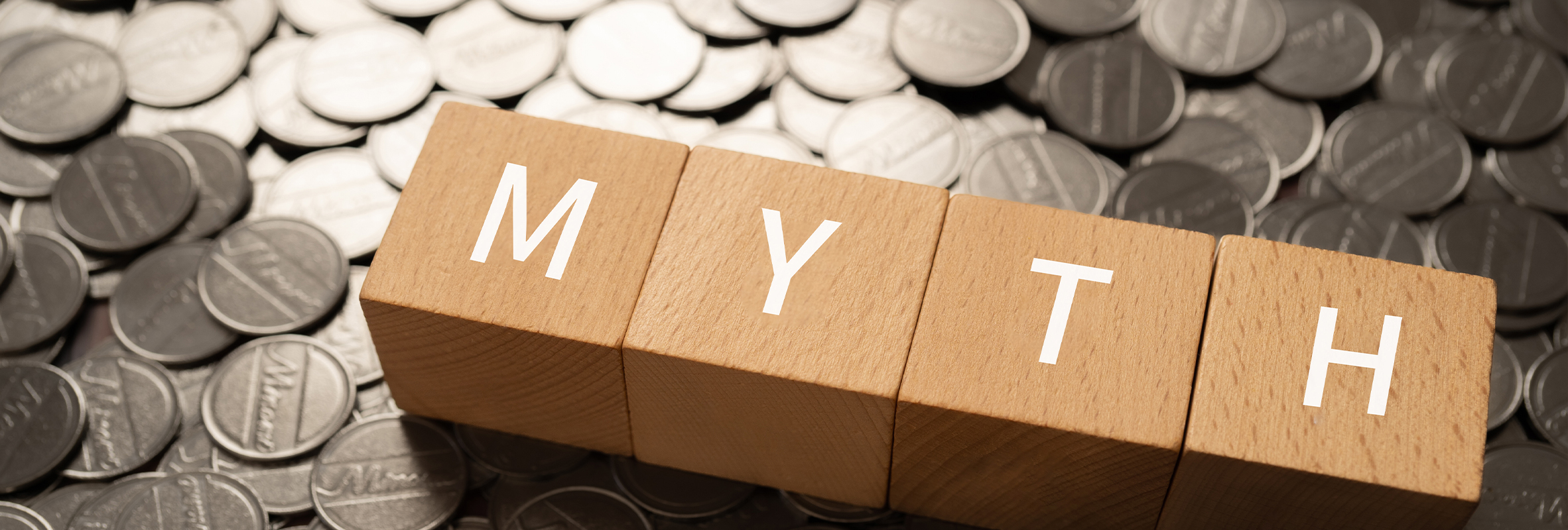 A wooden sign with the word “MYTH” spelled out in four separate blocks stands on a pile of assorted coins.